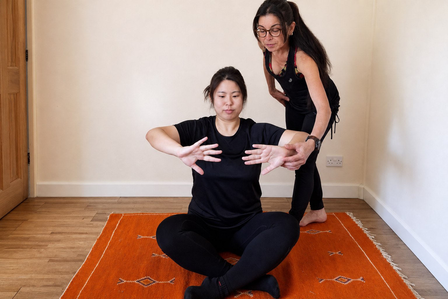 Participant seated cross-legged with her arms open while an instructor guides her hands